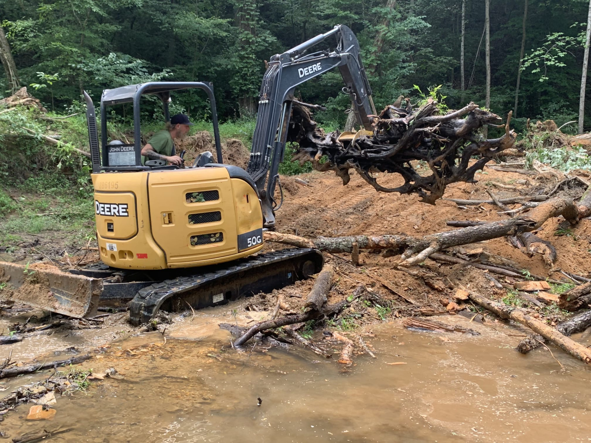 Mini excavator pulling a large stump from a creek bank